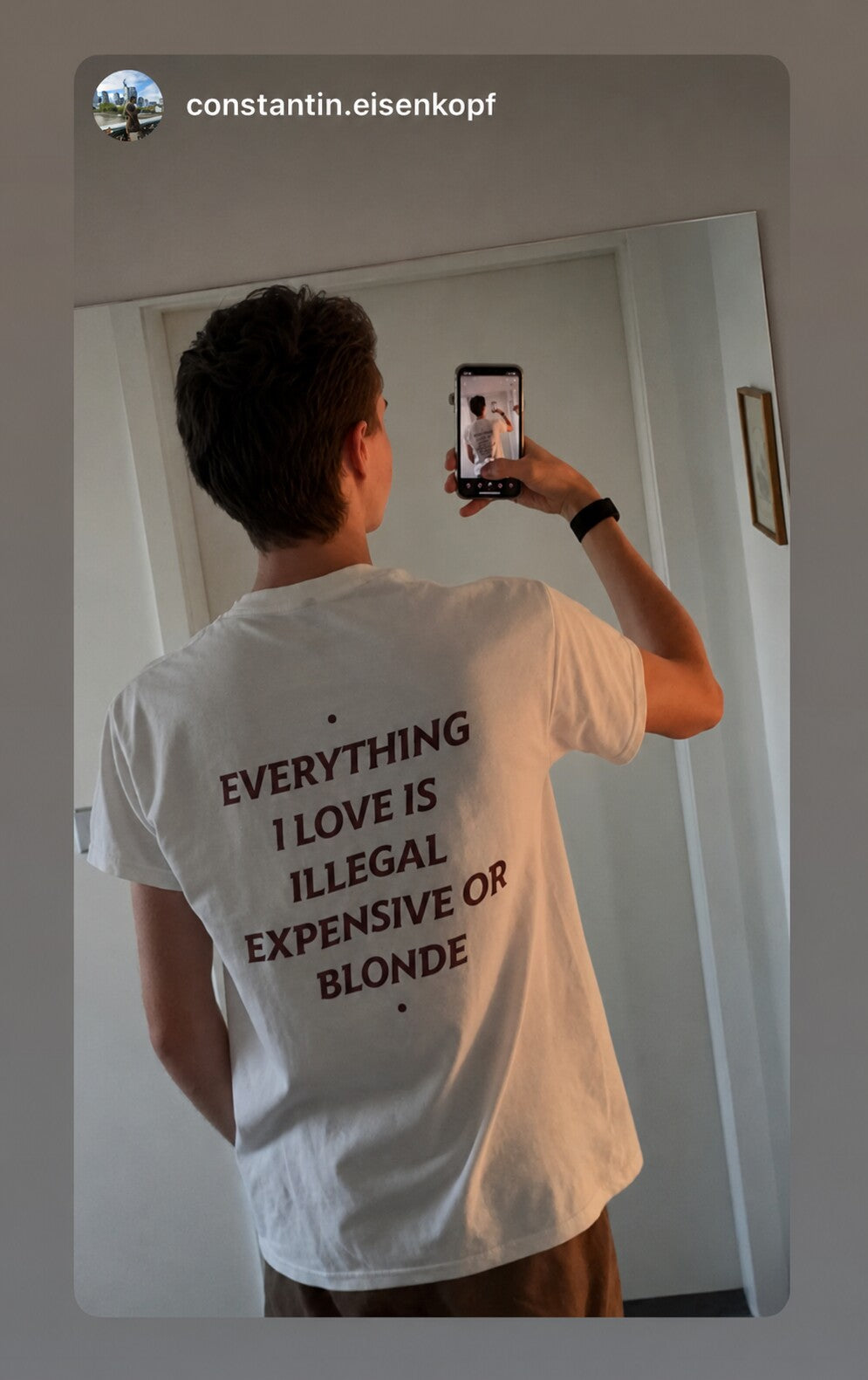Man taking a mirror selfie in a white “EVERYTHING I LOVE IS ILLEGAL EXPENSIVE OR BLONDE” T-shirt.